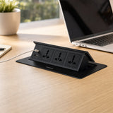 Desktop pop up socket recessed flush in an office desk, tilted open with a USB cable charging a laptop