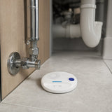 Water leak sensor placed on the floor beside pipework under a kitchen sink